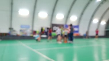 Badminton raketleriyle sahada antrenörün yanında duran bulanık çocuklar.