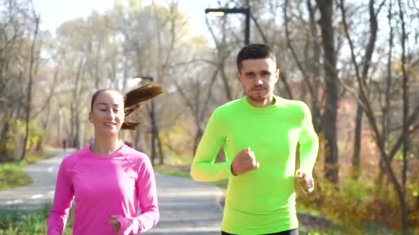 Happy athletic couple jogging in autumn park on sunny day — Stock Video