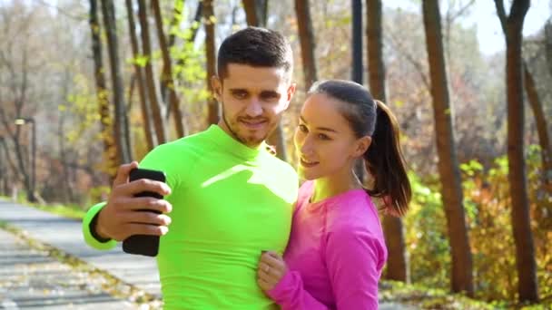 Gülümseyen atletik çift sonbahar parkında selfie çekiyorlar. — Stok video
