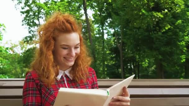 Jovial fille aux cheveux rouges riant de livre drôle dans le parc — Video