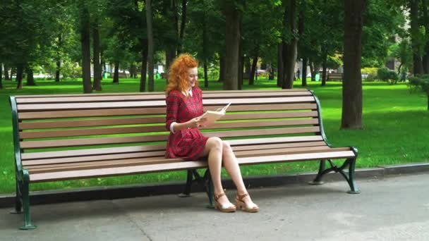 红头发女孩在公园里看有趣的书 — 图库视频影像