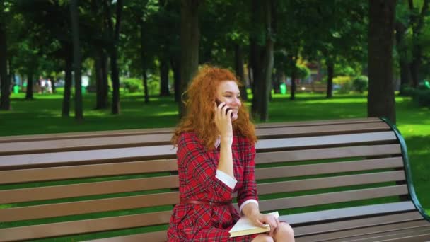 Jovial red haired girl talking on smartphone in park and laughing — Stock Video