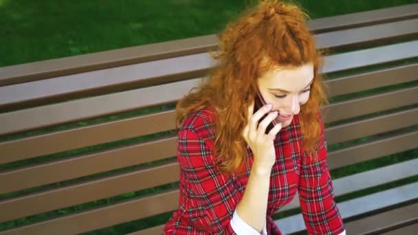 Glücklich schönes Mädchen, das auf Smartphone im grünen Park spricht — Stockvideo