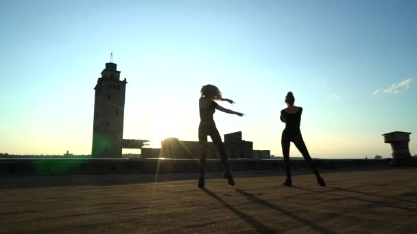 Силуэт девушек, танцующих парами на крыше на закате — стоковое видео