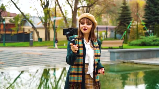 Parkta canlı yayın yapmak için Steadicam ve smartphone kullanan güzel kız vlogger — Stok video