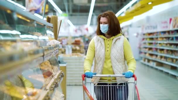 Wanita muda bertopeng medis dan sarung tangan oleh rak-rak dengan kue segar di toko — Stok Video