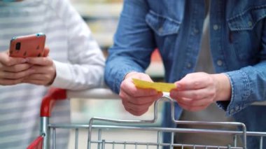 Süpermarkette alışveriş listesi ve akıllı telefonlu anne ve kızın elleri