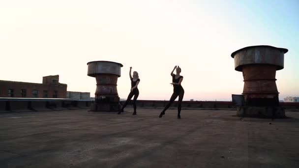 Chicas bonitas en trajes negros bailando en el techo industrial al atardecer — Vídeo de stock