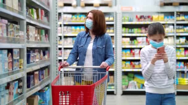 Madre e hija en máscaras caminando entre pasillos en la tienda de comestibles — Vídeos de Stock