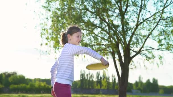 Маленькая девочка веселится с пластиковым диском в солнечном парке — стоковое видео
