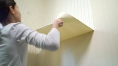 Küçük kız oturma odasında eski duvar kağıtlarını çıkarıyor.