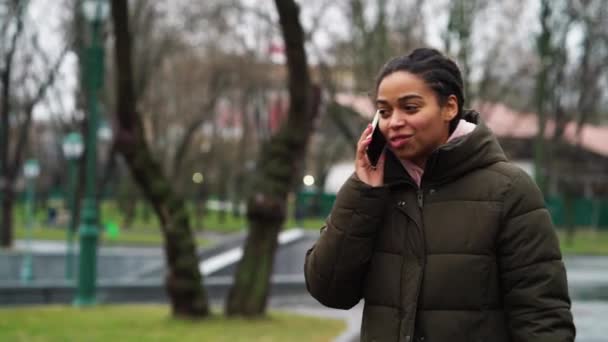 Amiable czarny dziewczyna mówi przez telefon w parku w zimną pogodę — Wideo stockowe