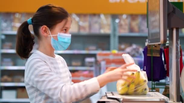 Kleines Mädchen in Maske wiegt Bananen im Supermarkt — Stockvideo