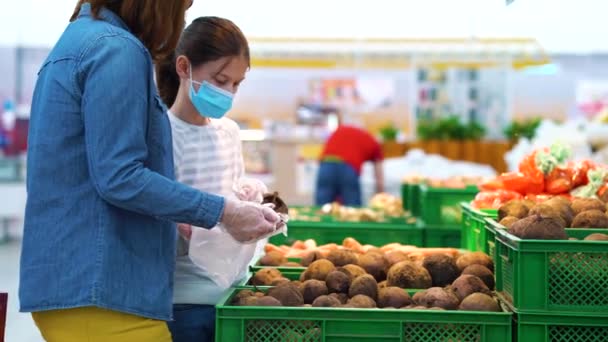 Mutter und Tochter in Masken und Handschuhen kaufen Gemüse im Supermarkt — Stockvideo