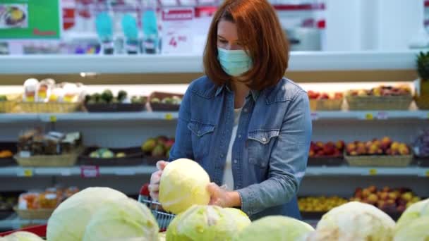 Mujer joven con máscara y guantes comprando repollo en el supermercado — Vídeos de Stock