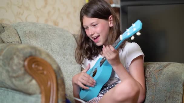 Mooi meisje spelen blauwe ukelele gitaar thuis — Stockvideo