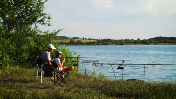 Отец и дочь сидят с удочками на берегу реки — стоковое видео