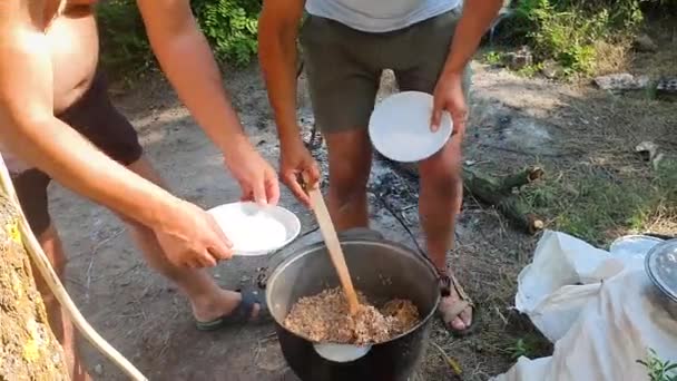 Wanderer servieren Brei in Metallschüssel am Lagerfeuer — Stockvideo