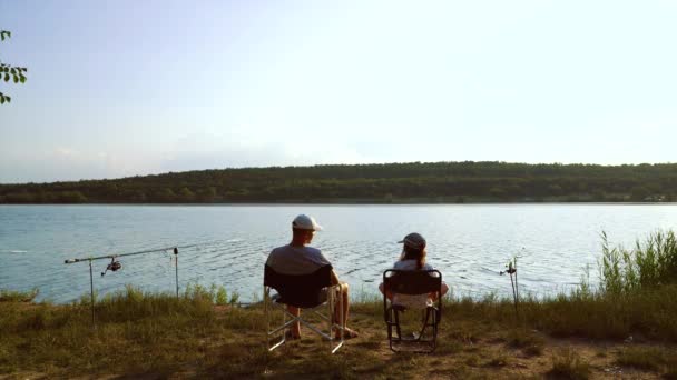 Far och barn sitter på älvstranden med fiskespön och pratar — Stockvideo