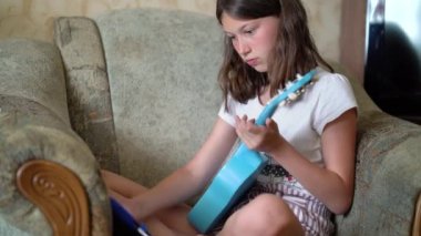 Küçük kız internet kursunu izliyor ve evde gitar çalıyor.
