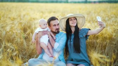 Mutlu anne buğday tarlasında sevimli bir bebekle ailesinin fotoğrafını çekiyor.