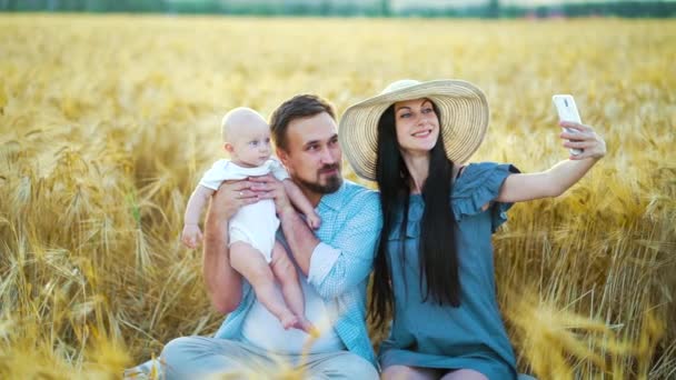 Lycklig mor tar selfie foto av sin familj med söt bebis i vetefält — Stockvideo