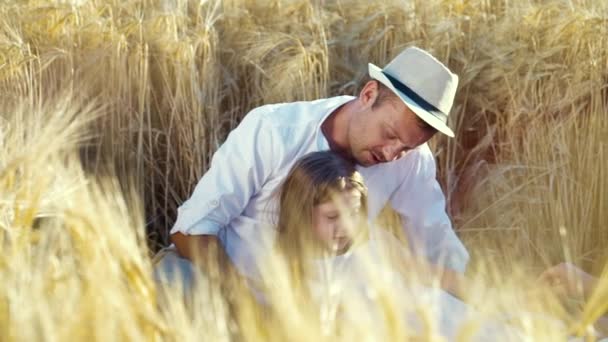 Familia feliz con hija pequeña haciendo un picnic en el campo de trigo en verano — Vídeo de stock