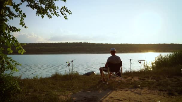 Gün batımında nehir kıyısında alkol içen balıkçı silueti. — Stok video