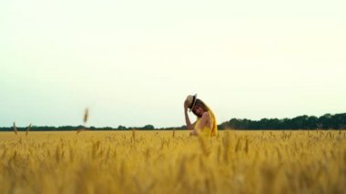 Romantik kız yazın buğday tarlasında hasır şapkayla oynuyor.