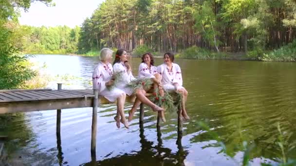 Young women in national Ukrainian clothes on pontoon bridge over river — Stock Video