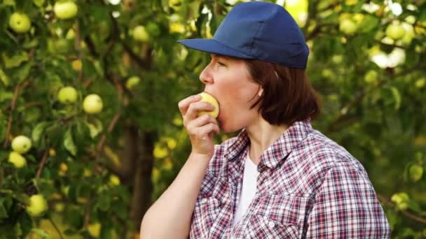 Młoda kobieta gryzie i żuje jabłko w sadzie — Wideo stockowe
