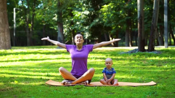 Mère et bébé pratiquant le yoga sur l'herbe verte dans le parc — Video