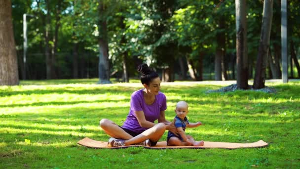 Mutter und Baby sitzen auf Yogamatte im grünen Park — Stockvideo