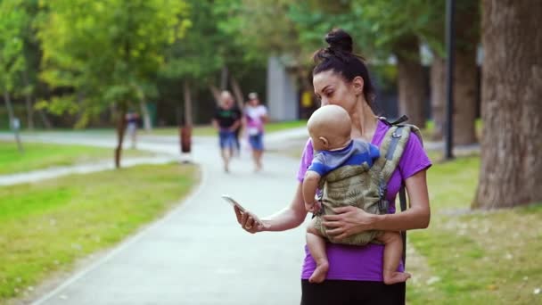 Fit femme en utilisant un smartphone tout en portant bébé en fronde — Video