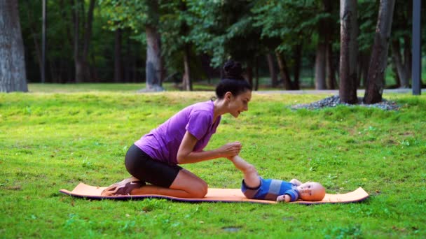 Мати робить дитячу гімнастику для свого маленького сина в зеленому парку — стокове відео