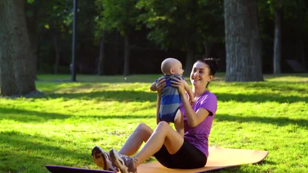 Fit moeder spelen met haar baby jongen na training in groen park — Stockvideo