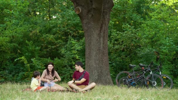 Сім'я має пікнік під деревом після їзди на велосипеді в лісі — стокове відео