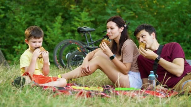 Aile, bisiklet sürdükten sonra doğada piknikte sandviç yiyor. — Stok video