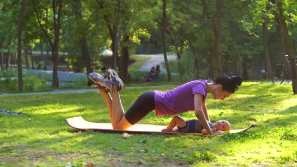 Fit moeder doen pushups en zoenen baby liggend op mat — Stockvideo