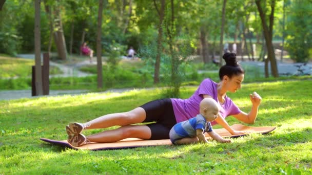 Sportowa matka trening na macie i dziecko bawiące się obok niej w parku — Wideo stockowe