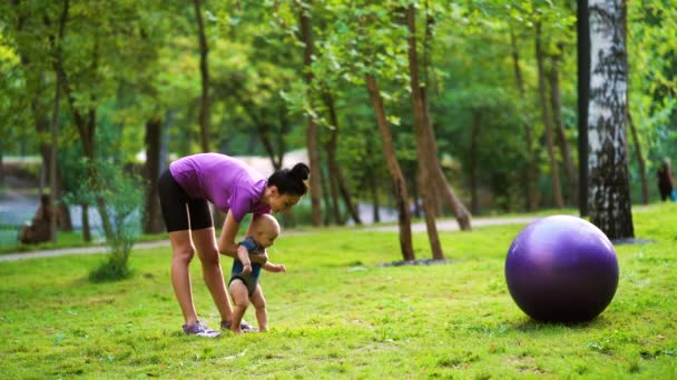 Дитина робить перші кроки за допомогою спортивної матері в парку — стокове відео
