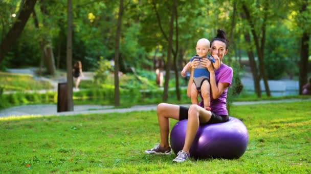 Sportig kvinna balansera med barnet på fitness boll i parken — Stockvideo