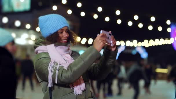 Joyful blogger afroamericana usando smartphone por la pista de patinaje en la noche — Vídeo de stock