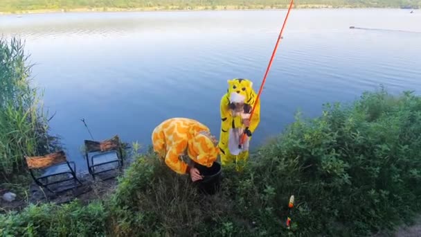 Nehir kıyısında pijamalı kızlar olta ve bir kova balık tutuyorlar. — Stok video