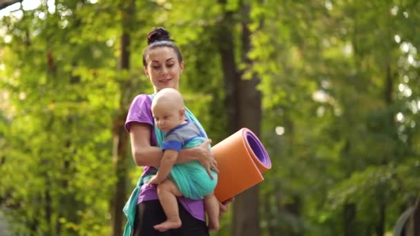 Yoga woman going to outdoor training with baby in sling — Stock Video