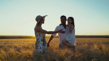 Sevgi dolu anne-baba ve kız gün batımında tarlada yürüyor.
