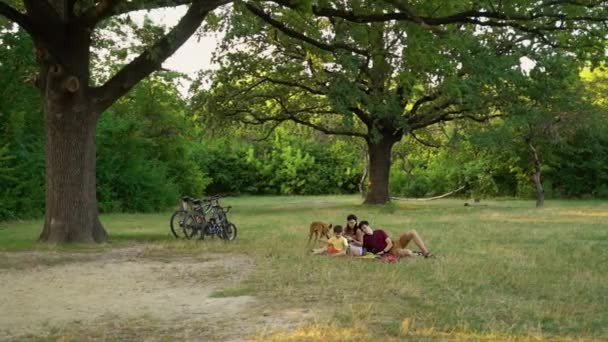 Familia con perro relajándose y haciendo picnic después de andar en bicicleta — Vídeo de stock