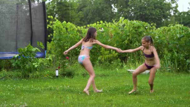 Niños felices en traje de baño girando juntos en el patio trasero bajo la lluvia — Vídeo de stock