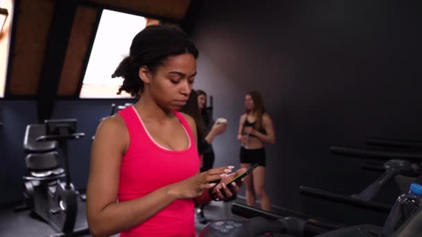 在健身房的跑步机上使用智能手机的黑人妇女 — 图库视频影像