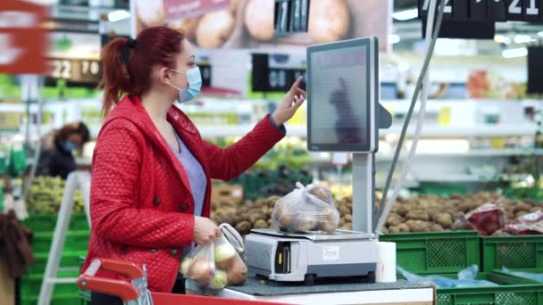 Молода жінка важить овочі в продуктовому магазині під час пандемії — стокове відео